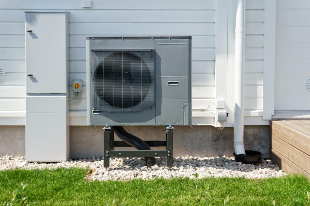 Air source heat pump installed on the exterior of a modern wooden house. Air source heat pump reduces heating costs and your home's carbon footprint.